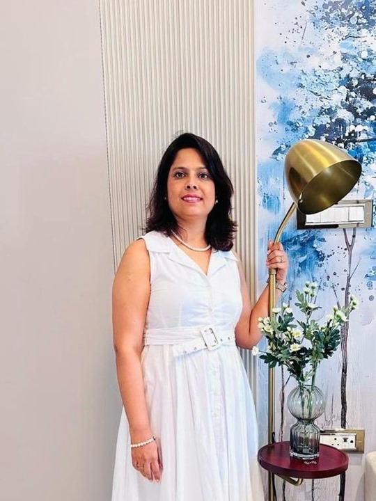 Sarika Kulkarni from SK Design Studio standing indoors with modern decor and floral arrangement.